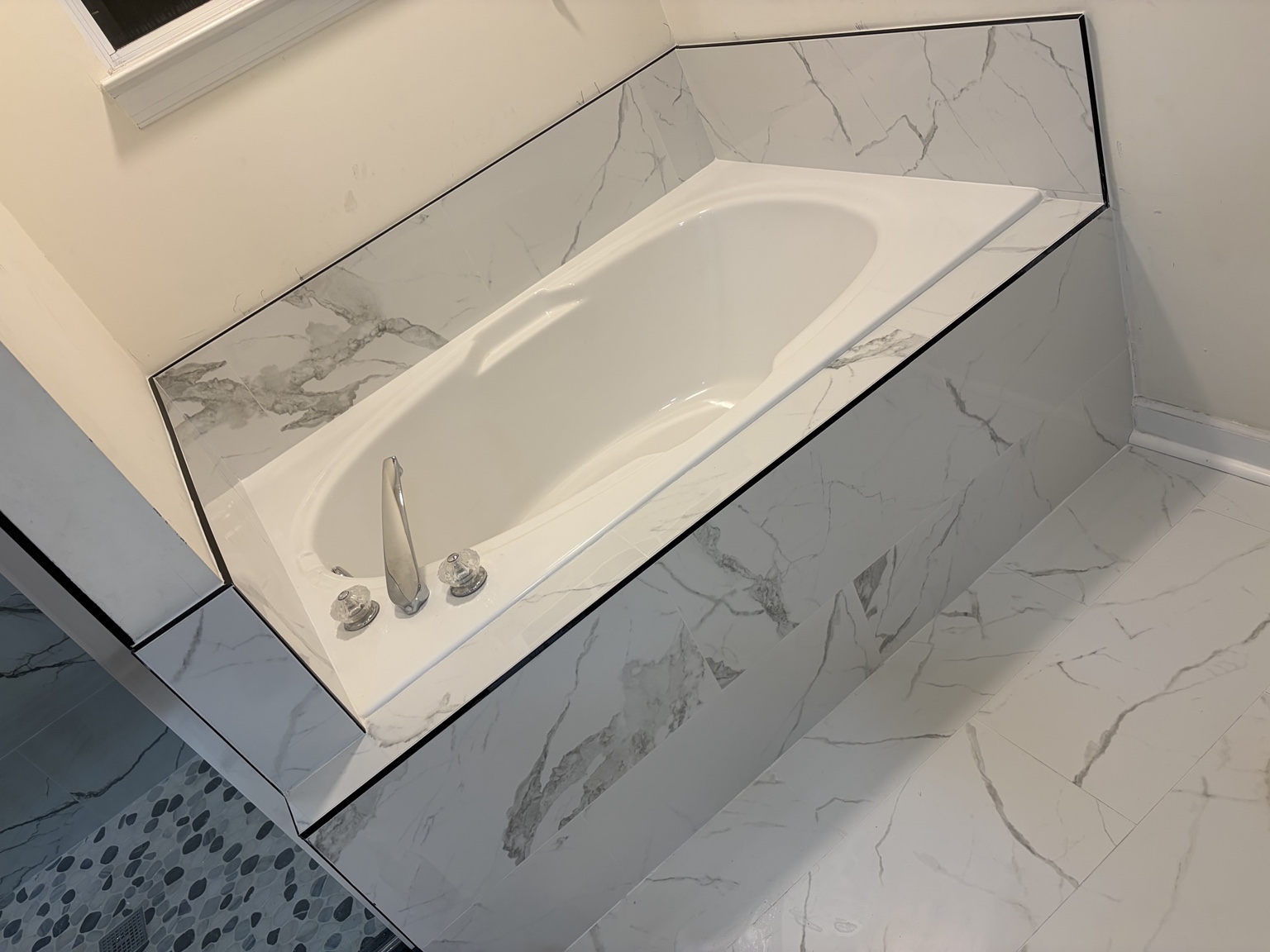 White bathtub with marble-look tile surround and bathroom floor tile
