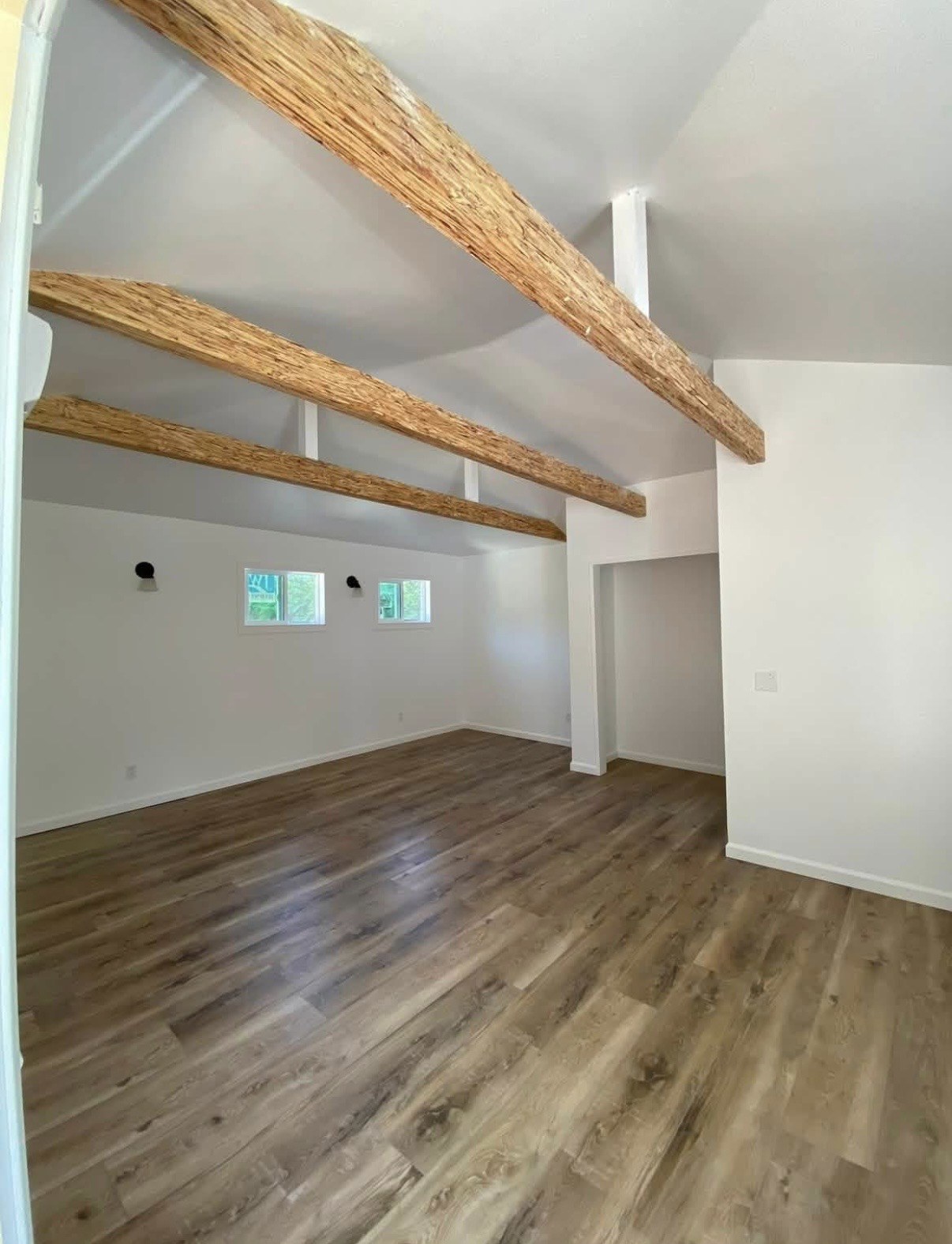 Finished room with exposed wood ceiling beams, white walls, and wood-look flooring