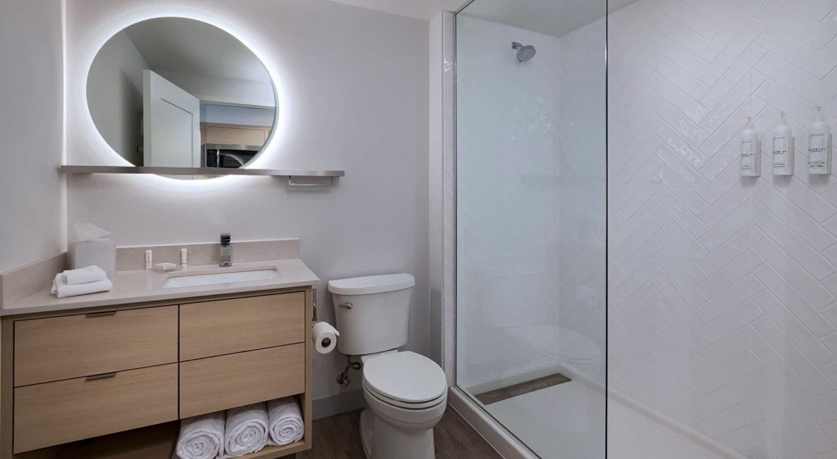 Modern bathroom with herringbone shower tile, glass enclosure, and wood vanity