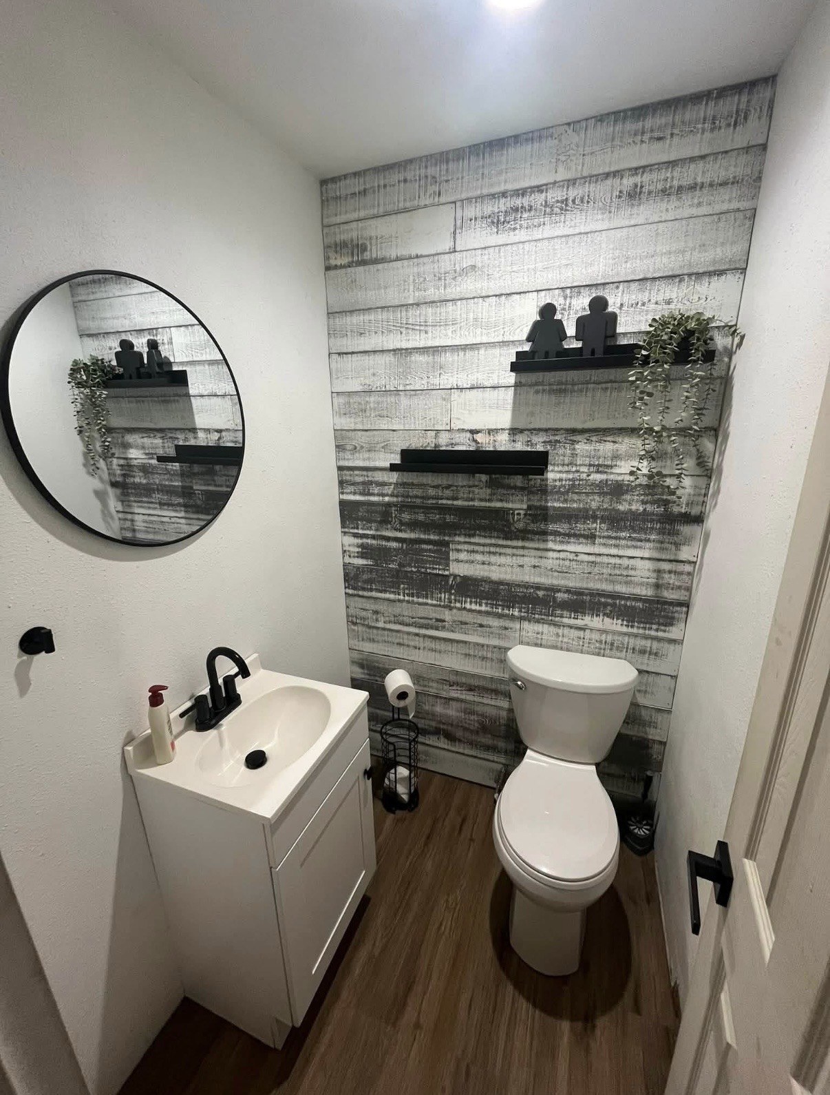 Powder room with a wood accent wall, white vanity, and black fixtures